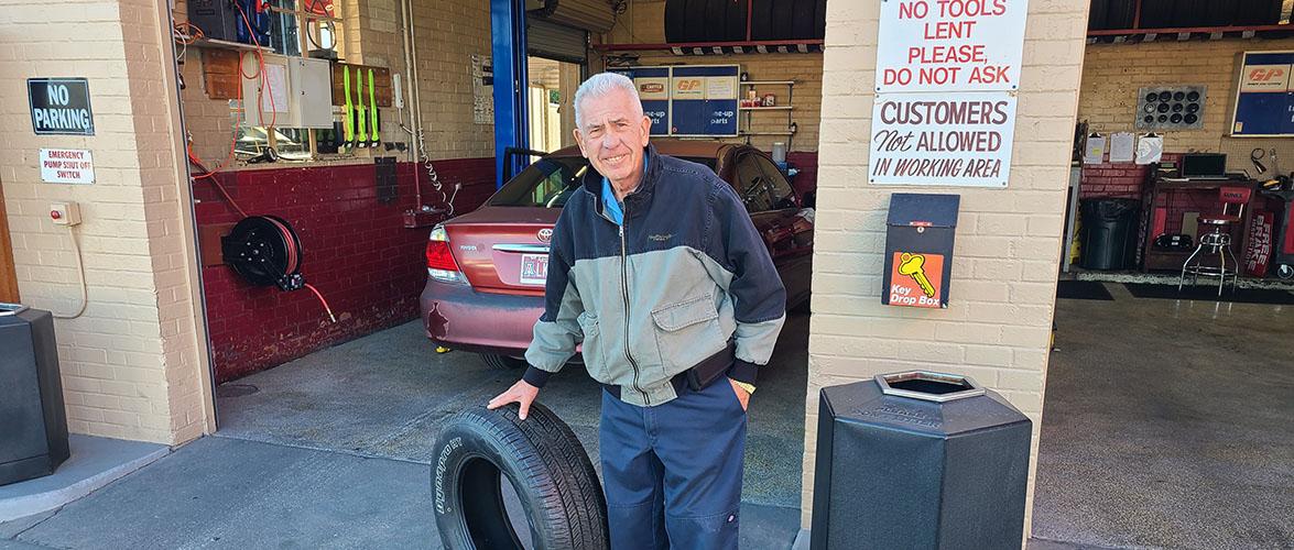 Technician outside the auto repair shop holding a tire.